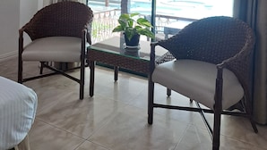 Una habitación con dos sillones de mimbre, una mesa de vidrio y una planta en maceta.