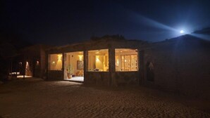 A stone building with a glass facade at night, illuminated by interior lights. - Hotel Tulor (San Pedro de Atacama)