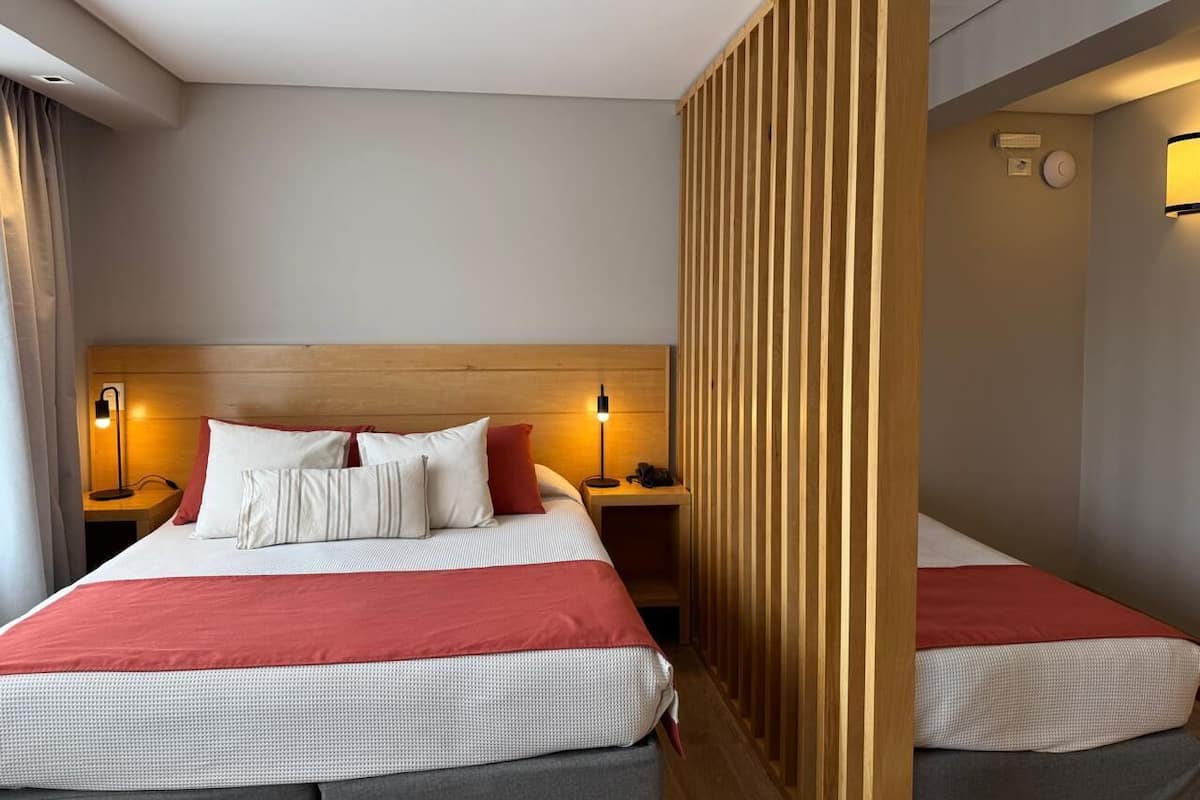Ein Hotelzimmer mit einem großen Bett, zwei Nachttischen, einem Holzkopfteil und einer Raumtrennwand.
