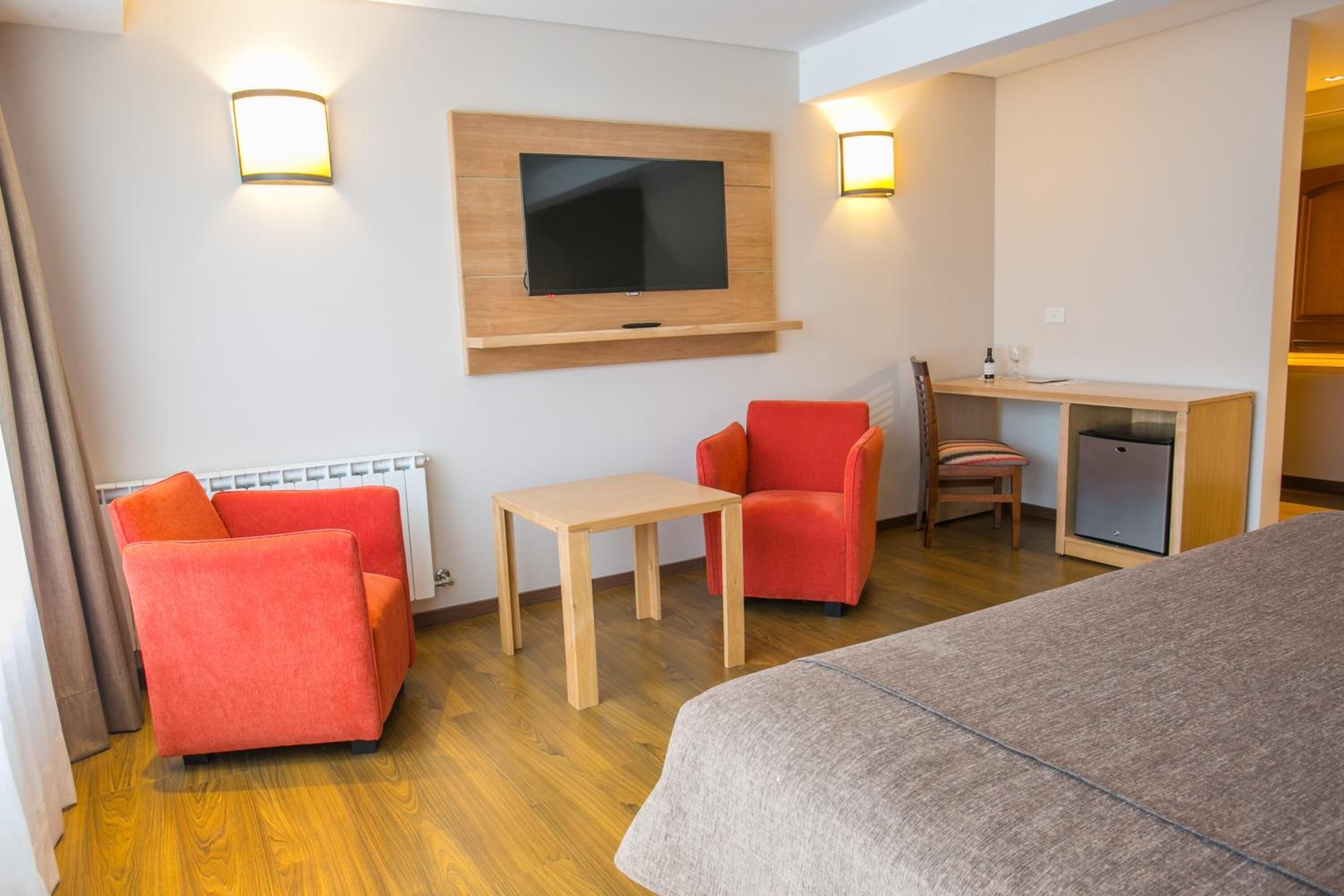 Habitación de hotel con cama, escritorio, televisor montado en la pared y dos sillas.