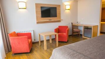 Habitación de hotel con cama, escritorio, televisor montado en la pared y dos sillas.