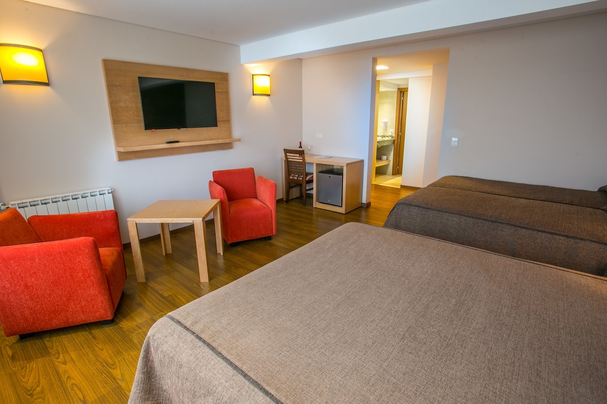 Ein Hotelzimmer mit an der Wand montiertem Fernseher, einem kleinen Schreibtisch mit Stuhl, einem roten Sofa und zwei Betten.