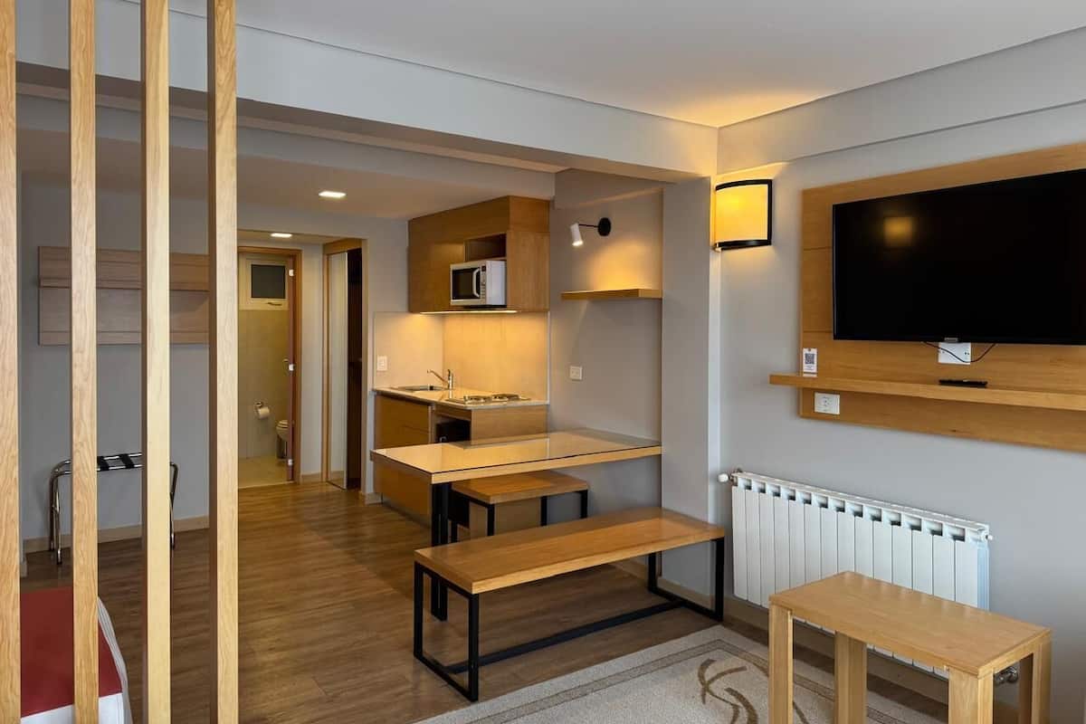 Eine kompakte Küche mit Mikrowelle, Spüle und Holzschränken. In der Mitte befindet sich eine Sitzbank und ein kleiner Tisch.