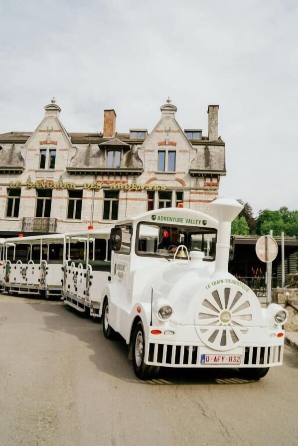Un autobús turístico blanco con la leyenda 'Adventure Valley' estacionado frente a un edificio histórico de fachada de piedra y numerosas ventanas.