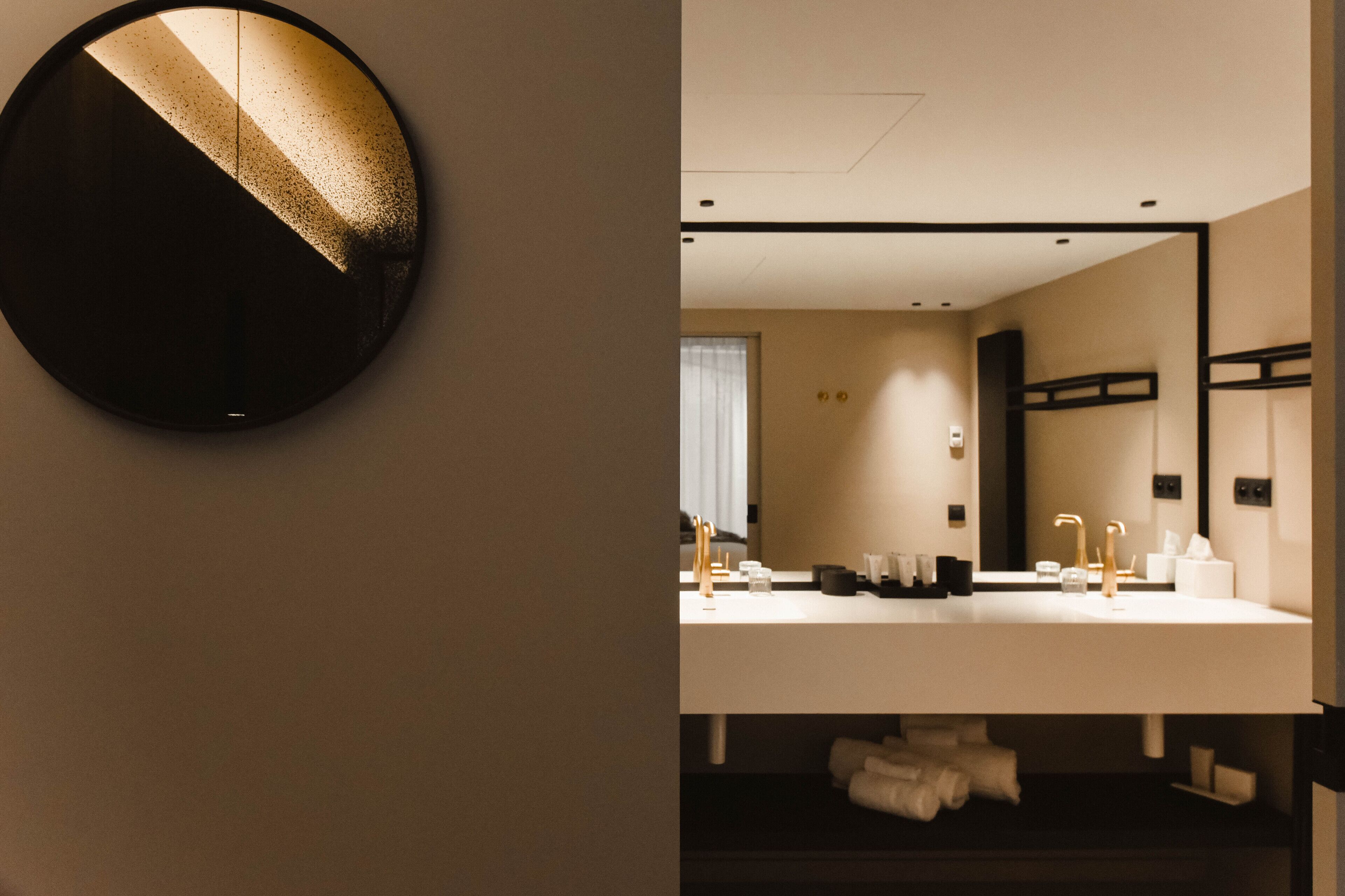 Ein modernes Badezimmer mit rundem Spiegel, doppelter Spüle und Handtuchhalter.