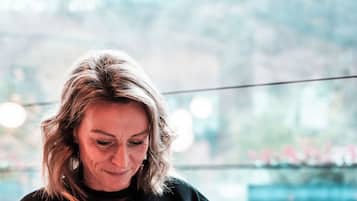 Une personne est assise à une table, devant un verre d’eau, une assiette de nourriture et une tasse de café.