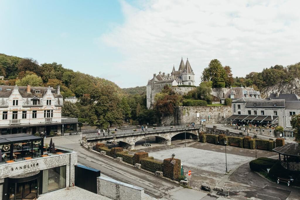 A historic castle on a hill overlooking a town square with a bridge, a restaurant, and a building labeled "SANGLIER."