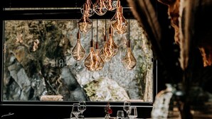 Interior de restaurante con un amplio ventanal, una mesa servida con copas de vino y una lámpara colgante original.