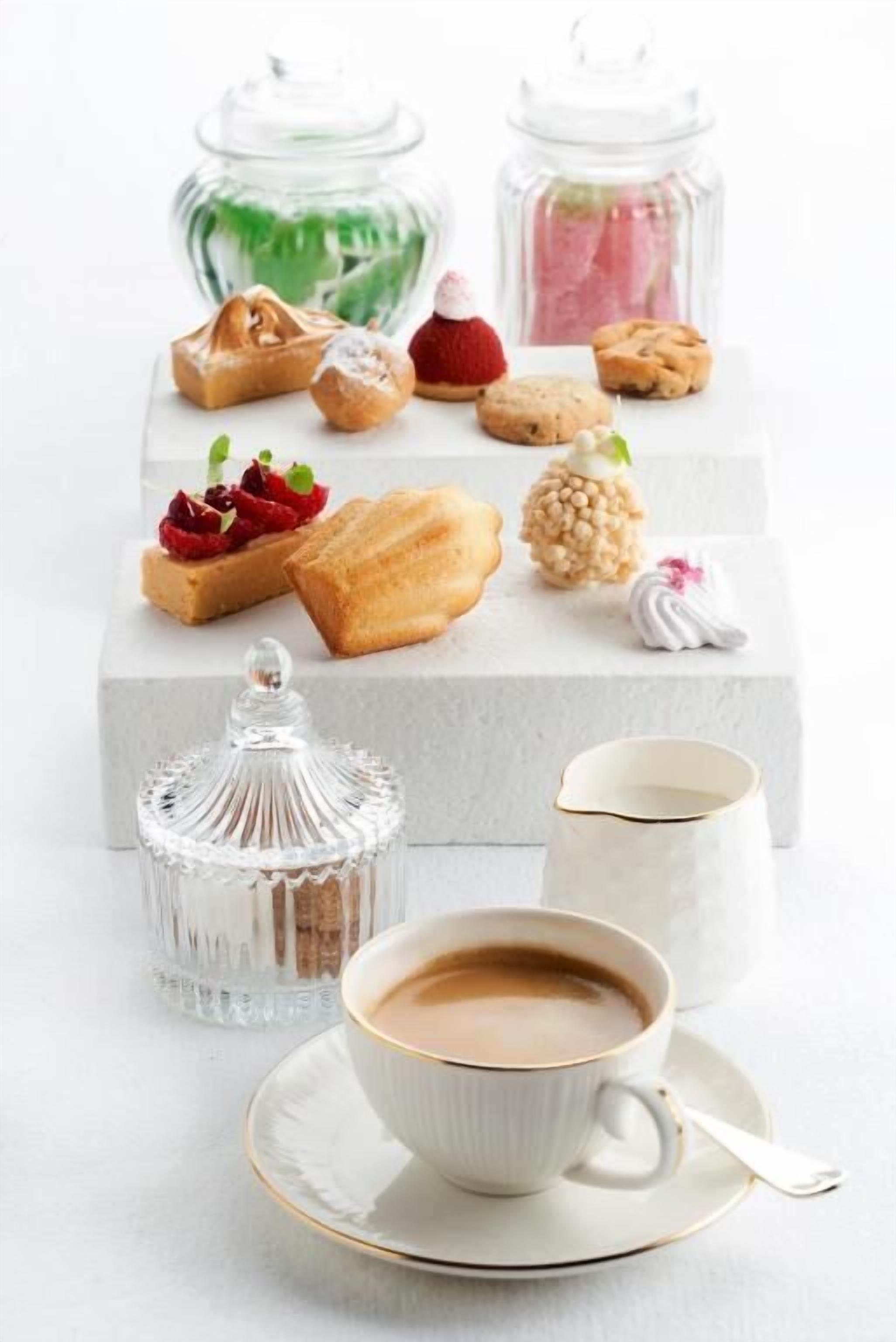 A selection of pastries and a cup of coffee on a white table, with two glass jars in the background.