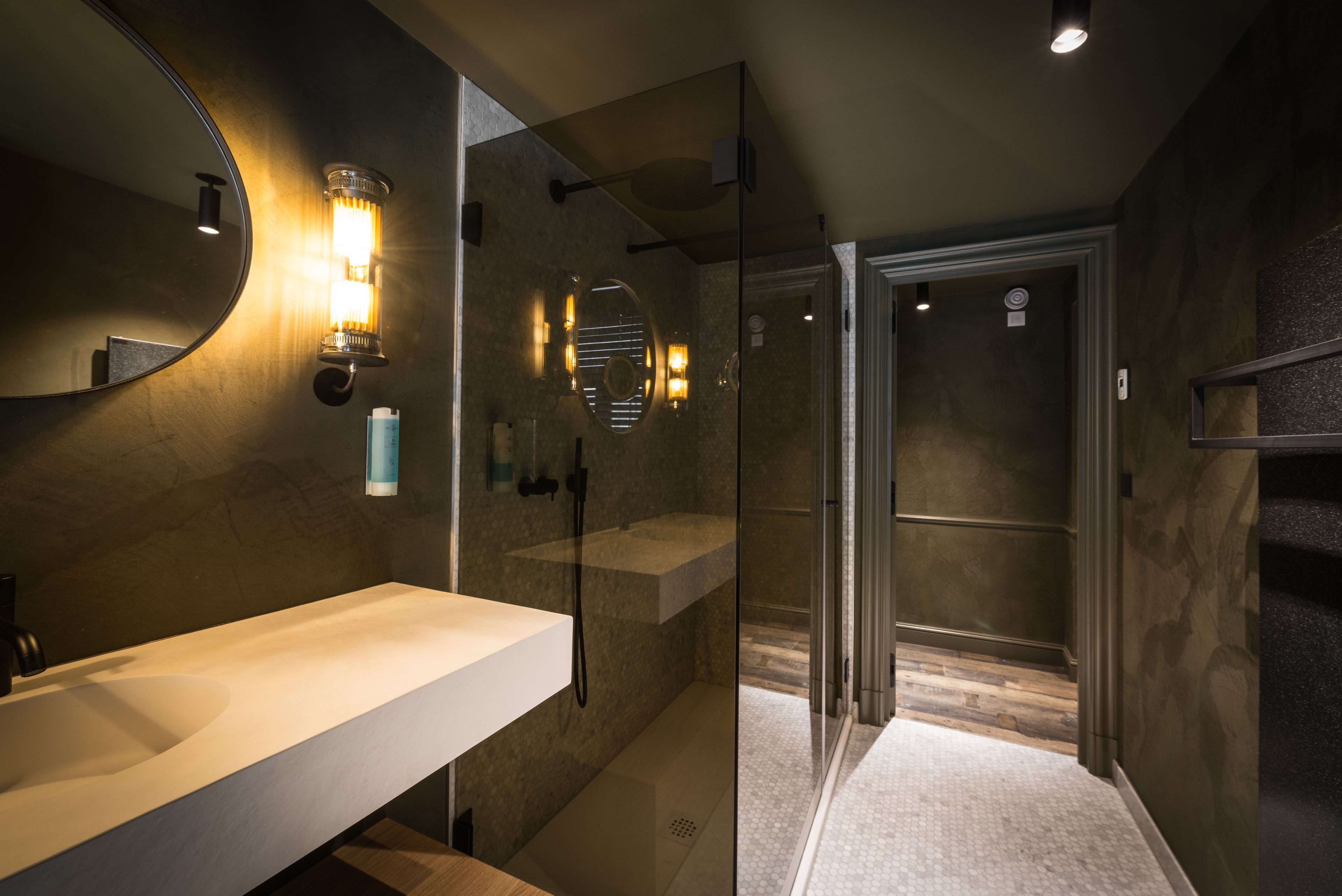 Un baño moderno con un espejo grande, un lavamanos blanco y una zona de ducha con paredes de vidrio.