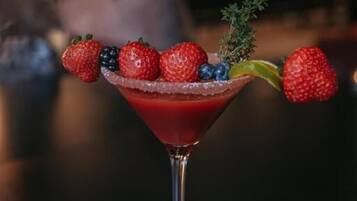 A martini glass with a red drink, garnished with strawberries and blueberries, and a sprig of thyme.