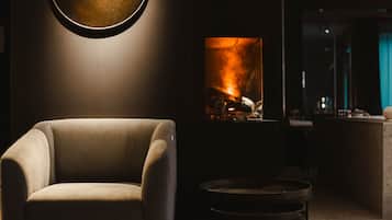 Una sala de estar moderna con un sillón cómodo, una lámpara redonda fijada a la pared y una chimenea con leña y llamas a la vista.