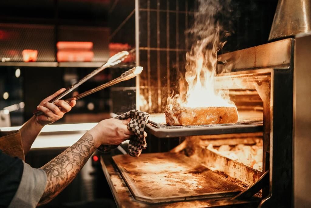 A person using tongs to handle a hot item inside an oven.