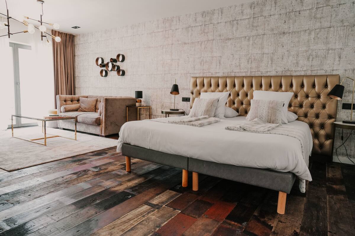 A modern bedroom with a tufted headboard, a large bed, a sofa, a coffee table, and a patterned rug.