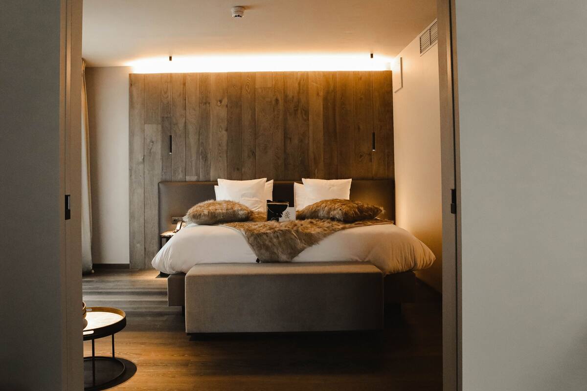 A modern bedroom with a wooden headboard, a bed with white linens and two pillows, a bedside table, and a small round table.