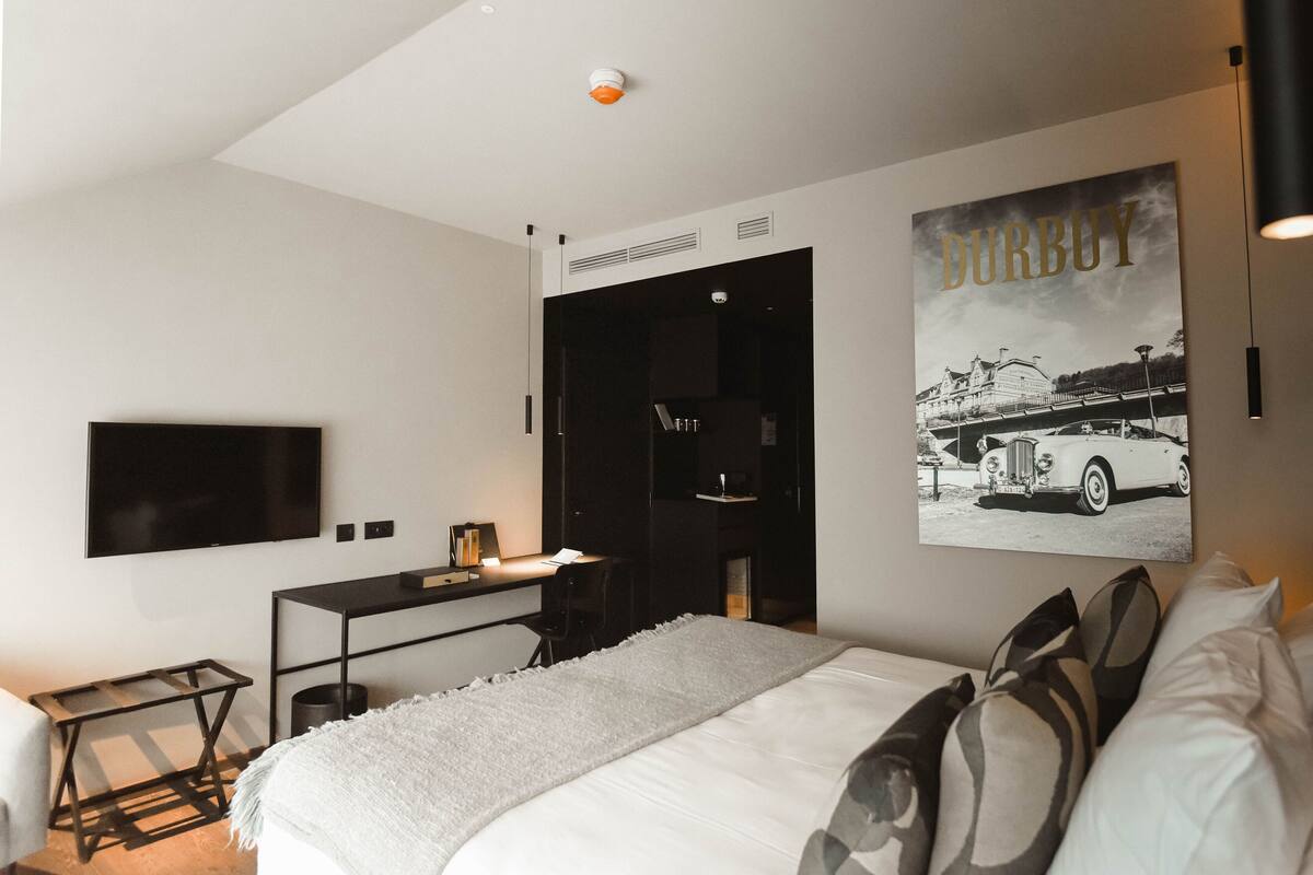 A modern hotel room with a large bed, a desk, and a flat-screen TV mounted on the wall.