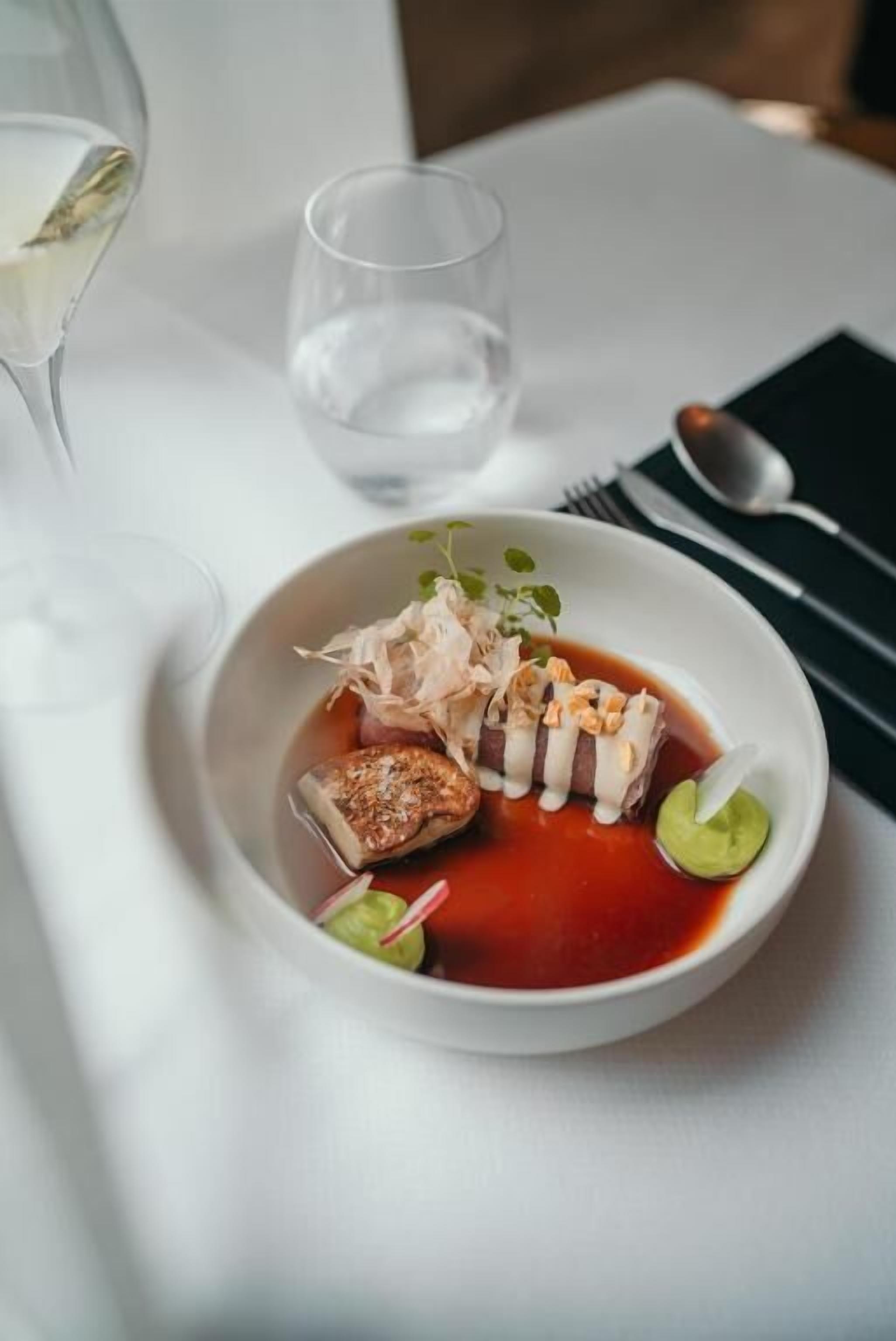 Una mesa blanca con un tazón de comida, un vaso de agua y un juego de tenedor y cuchara.