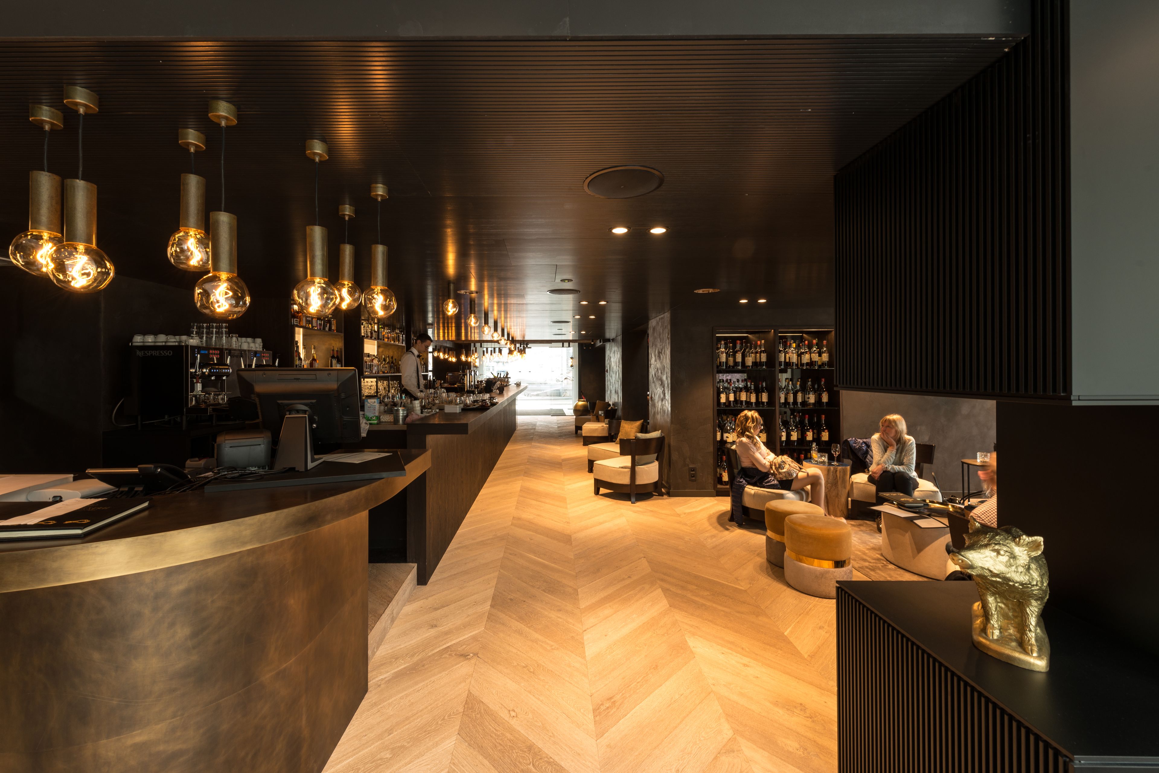 Un área de bar moderna con suelo de madera en espiga, luces colgantes y una barra.