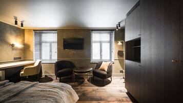 Un dormitorio moderno con una cama, un escritorio, dos sillones, una mesita redonda y un televisor montado en la pared.