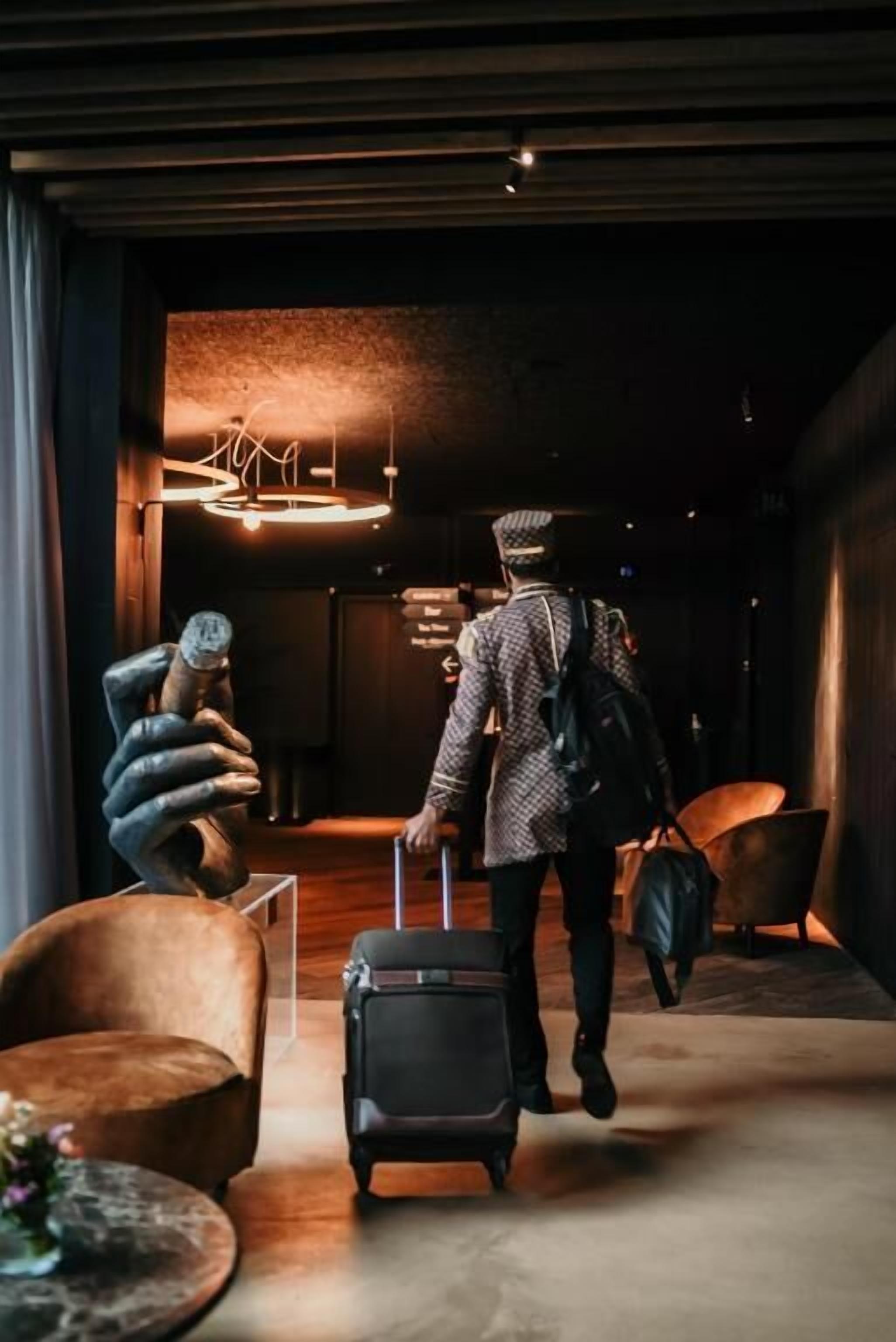 A person with a suitcase walking through a lobby with a modern design, including a unique sculpture and a stylish chandelier.