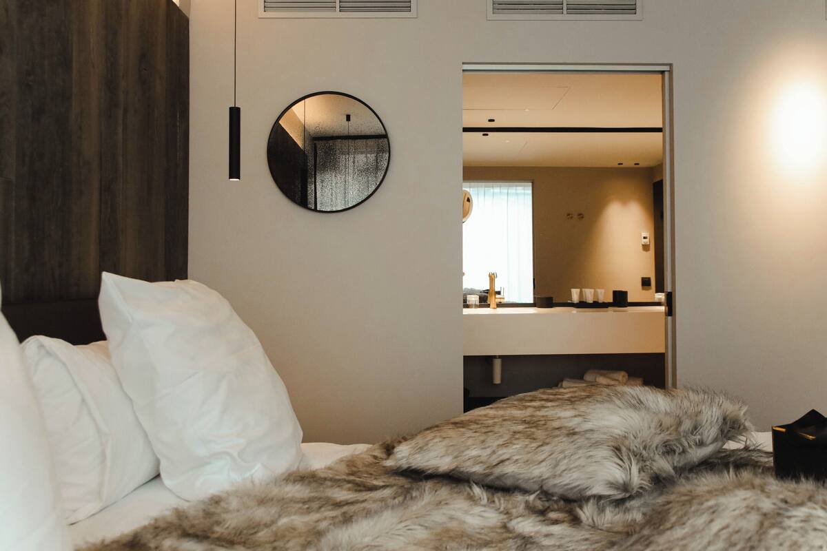 A modern bedroom with a large bed, a round mirror, and a built-in wardrobe.