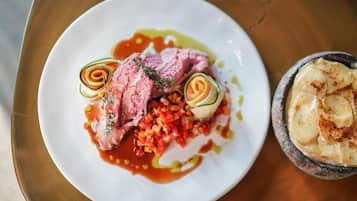 A plate of food with sliced meat, vegetables, and a small bowl of what appears to be a potato dish.