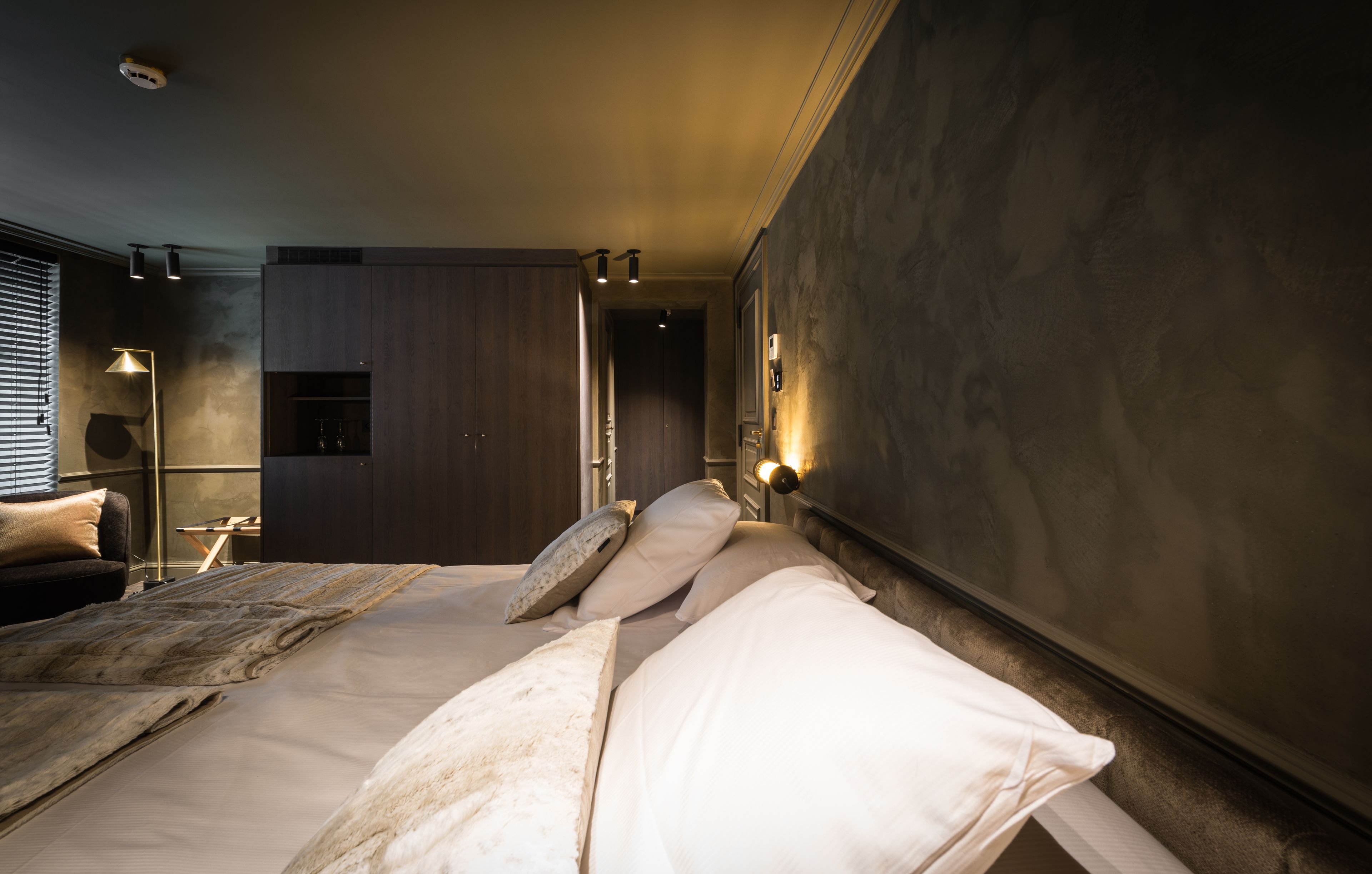 A modern bedroom with a large bed, bedside tables, a wardrobe, and a view of a kitchen area.