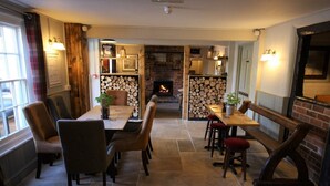 A cozy dining area with a fireplace, wooden furniture, and a stone floor. - The Carpenters Arms (Newbury)
