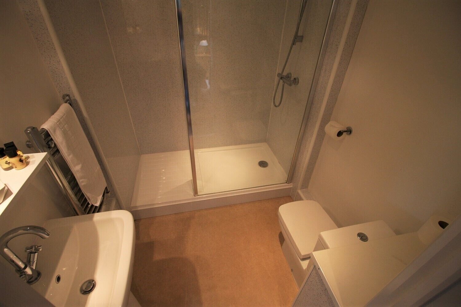 Un baño con ducha de vidrio, un lavamanos y dos inodoros.