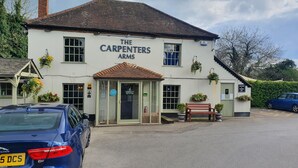 A building named 'The Carpenters Arms' with a traditional facade, a car parked in front, and a bench outside. - The Carpenters Arms (Newbury)