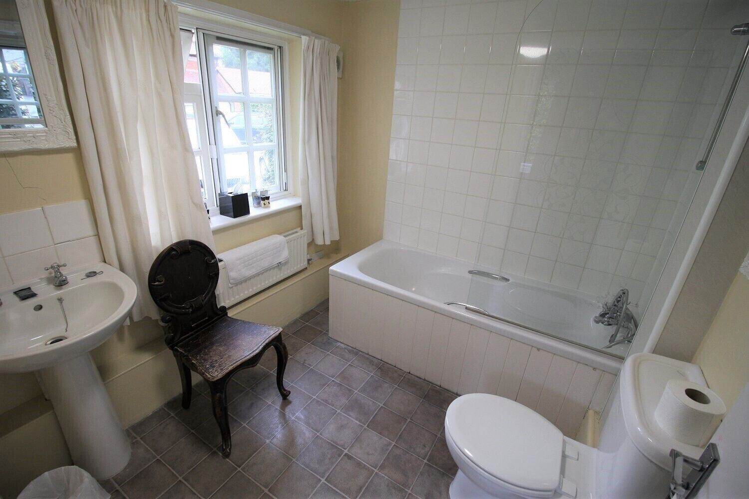 Une salle de bain équipée d’une baignoire, de toilettes, d’un lavabo et d’une fenêtre avec des rideaux.