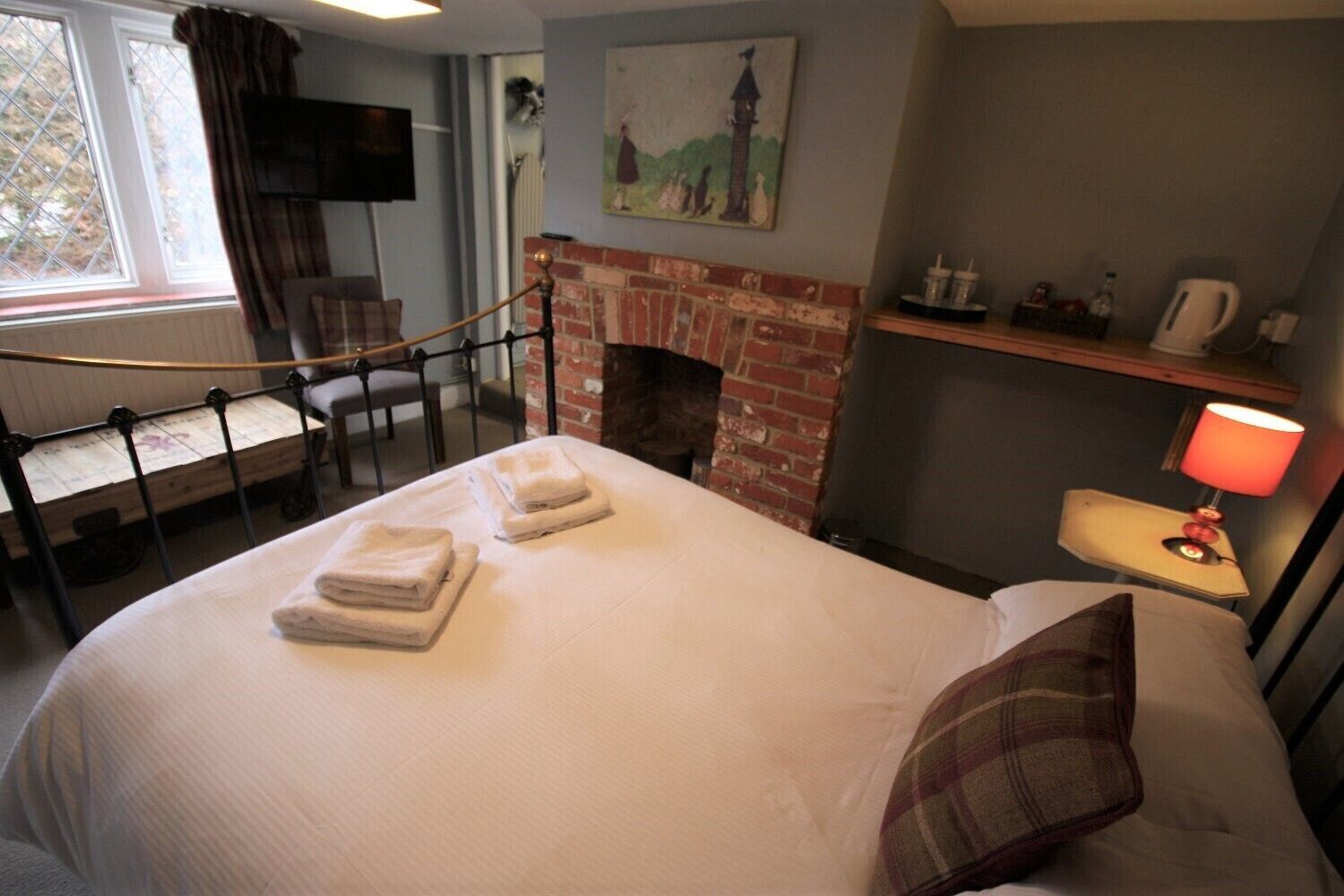 Una habitación de hotel con cama, chimenea, televisor montado en la pared y ventana con cortinas.