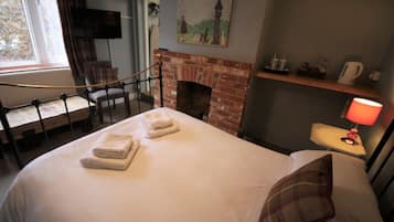 Una habitación de hotel con cama, chimenea, televisor montado en la pared y ventana con cortinas.