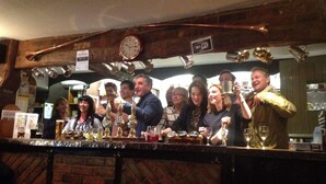 A group of people at a bar with a clock on the wall and various bottles of beer. - The Carpenters Arms (Newbury)