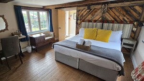 A bedroom with a bed, a desk, a chair, a window, and a wooden ceiling. - The Carpenters Arms (Newbury)