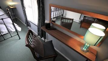 A hotel room with a wooden desk, a chair, a mirror, a lamp, and a bed with a headboard.