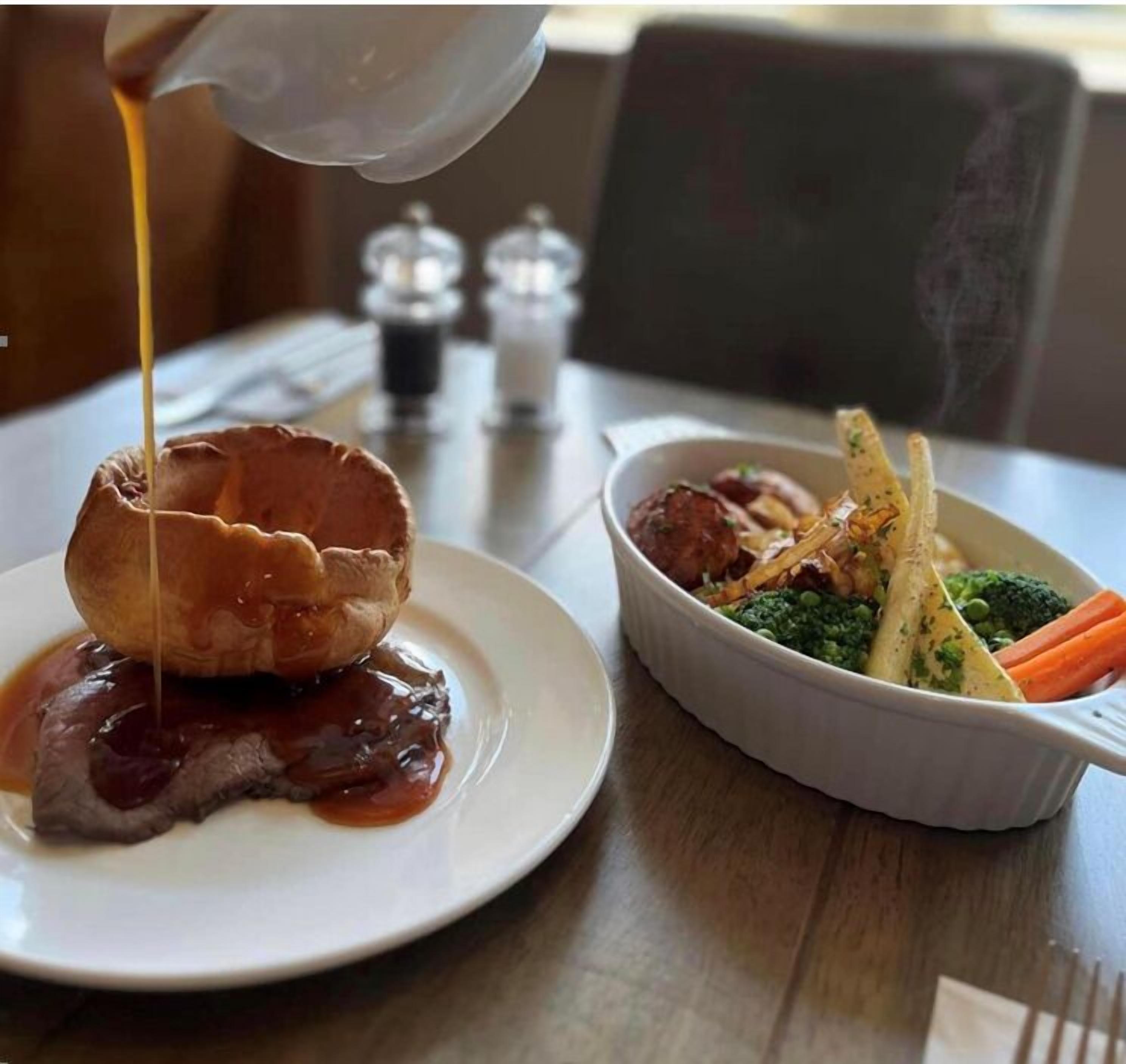 A plate with a meat dish, a bowl of vegetables, and a sauce being poured.
