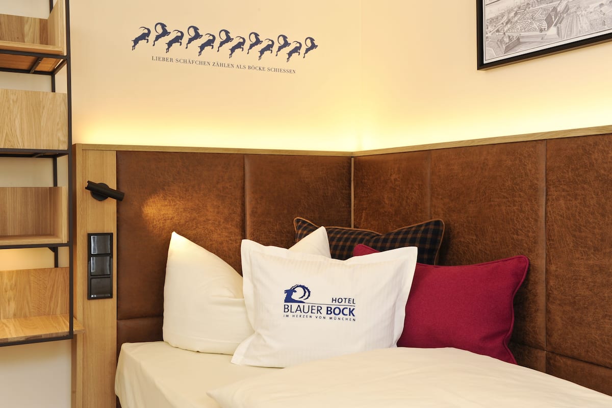 A hotel room with a brown headboard, a bed with white and red pillows, and a wall-mounted light.