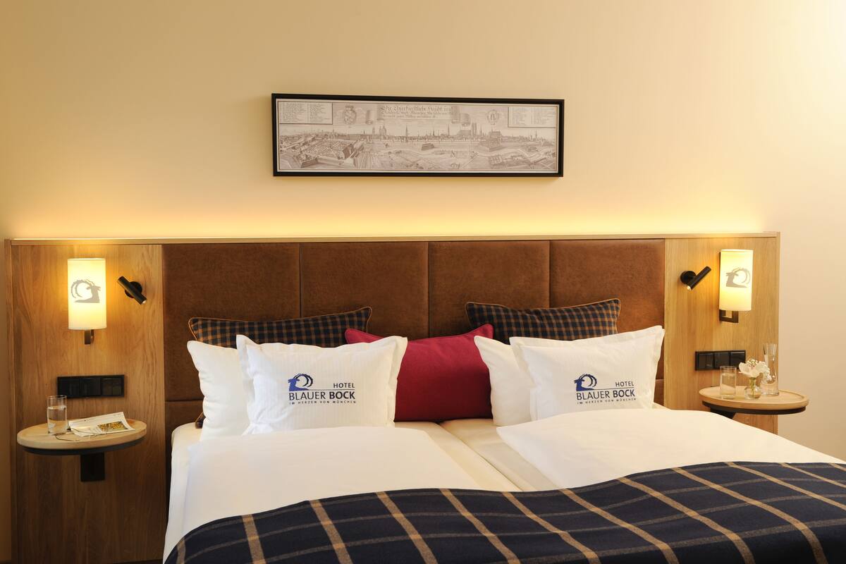A hotel room with a large bed, two bedside tables, a framed picture on the wall, and a sign indicating the hotel name.