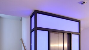 Un moderno ascensor con un diseño elegante, ubicado junto a una escalera de madera con barandilla.