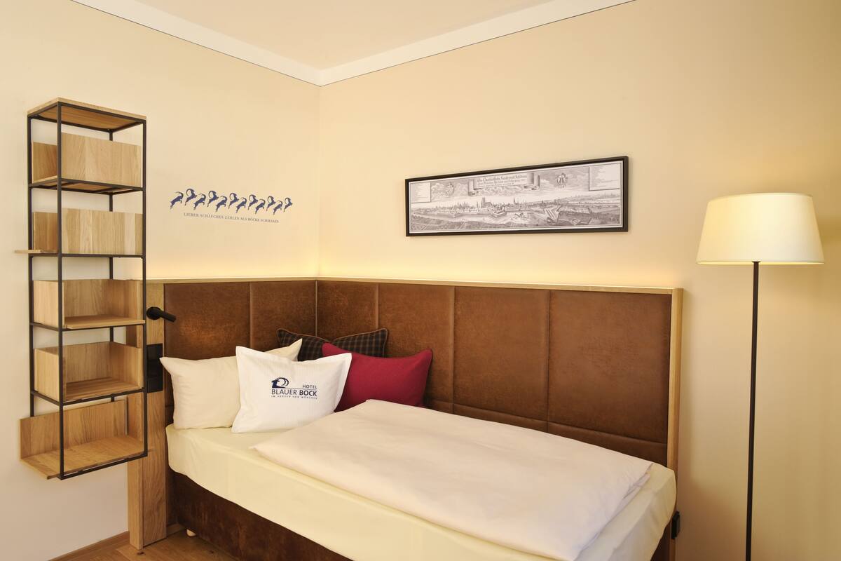 A hotel room with a bed, a wooden shelf unit, a framed picture, and a lamp.