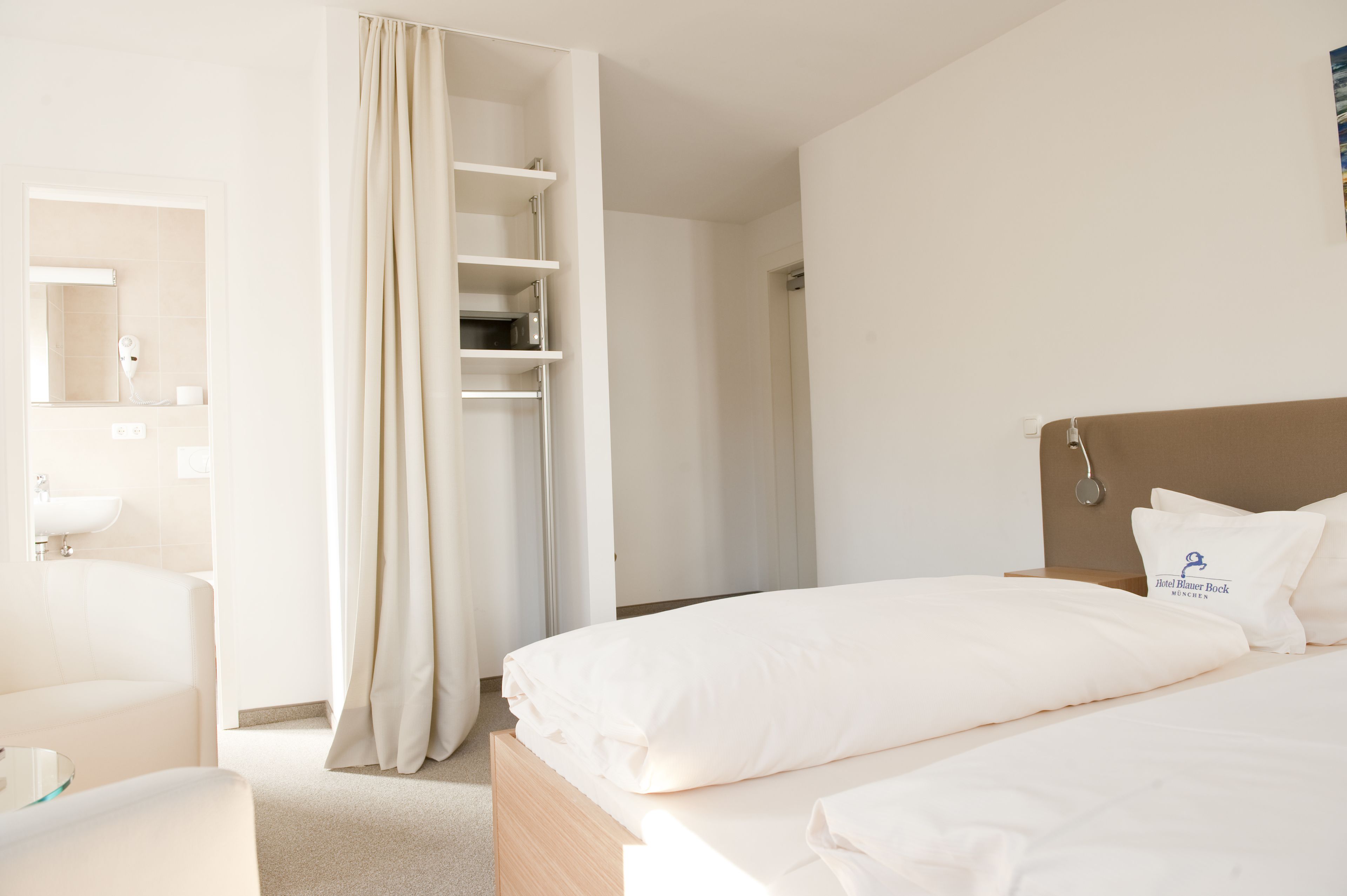 Une chambre d’hôtel comprenant un lit, une table de chevet, un miroir, une salle de bain avec un lavabo et un espace douche.