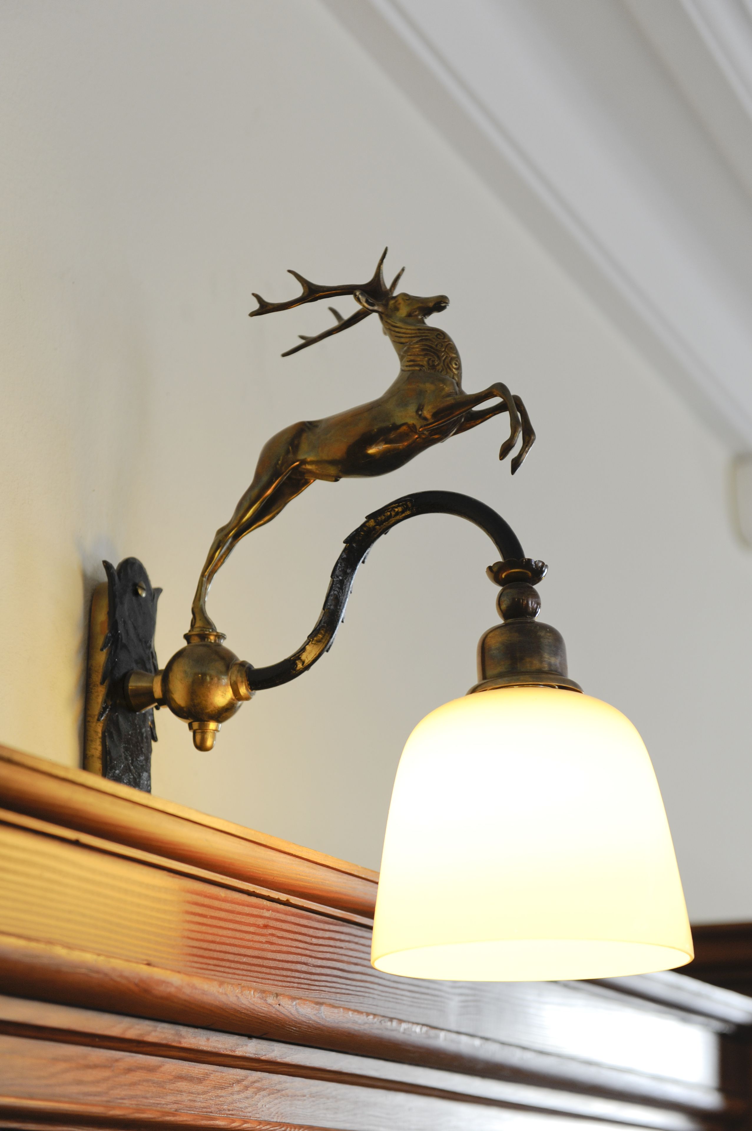 A brass wall-mounted lamp with a deer figurine and a white lampshade.
