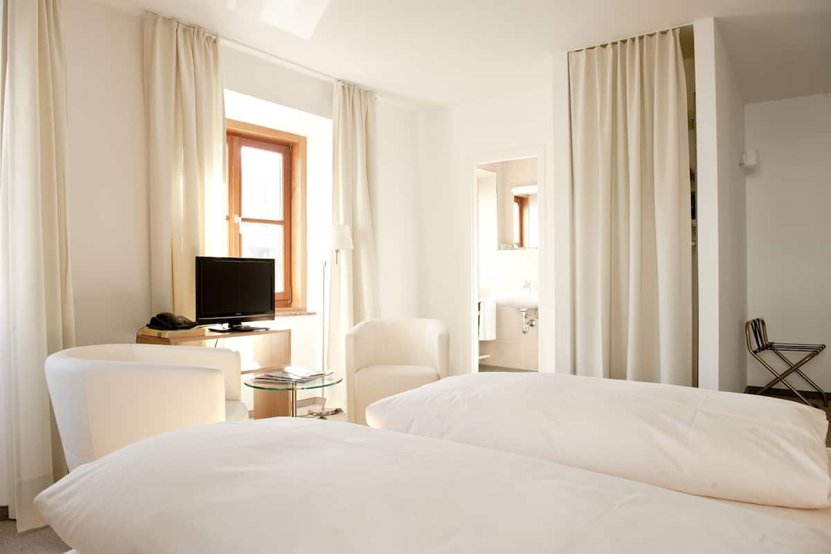 A hotel room with two beds, a TV, a desk with a lamp, and a chair.