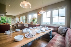 A spacious kitchen with a long wooden table set for dining, large windows offering a view, and a cozy seating area with a plaid sofa. - The Three Daggers (Westbury)