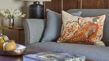 A cozy living room with a grey sofa, a wooden coffee table, a lamp, a framed picture, and a vase with flowers.