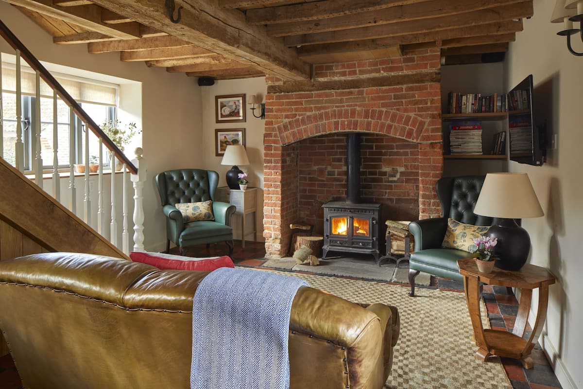 A cozy living room with a brick fireplace, leather furniture, and a bookshelf.