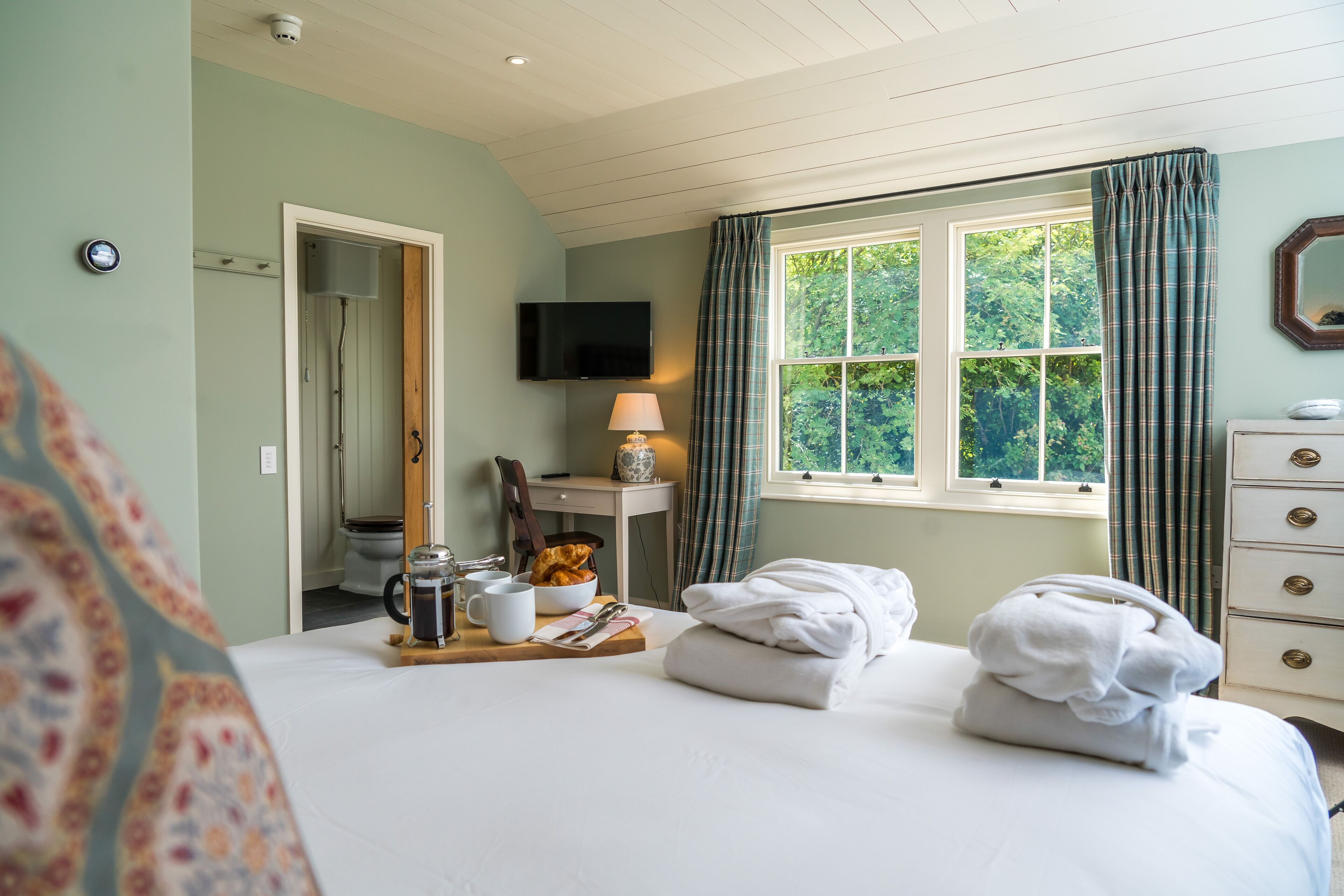 A hotel room with a bed, a desk with a lamp, a television, and a window with curtains.