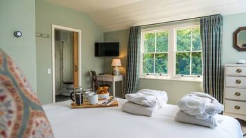 A hotel room with a bed, a desk with a lamp, a television, and a window with curtains.