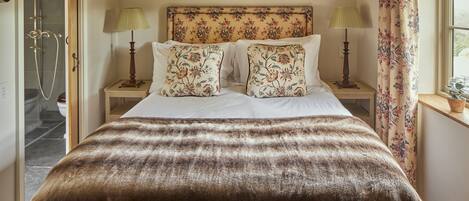 A bedroom with a large bed, floral headboard, two bedside lamps, and a window with curtains.
